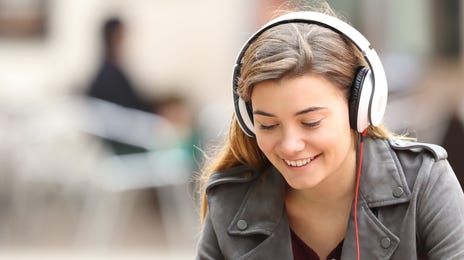 Young woman sitting outside with her headphones on and attending an online group class from a tablet