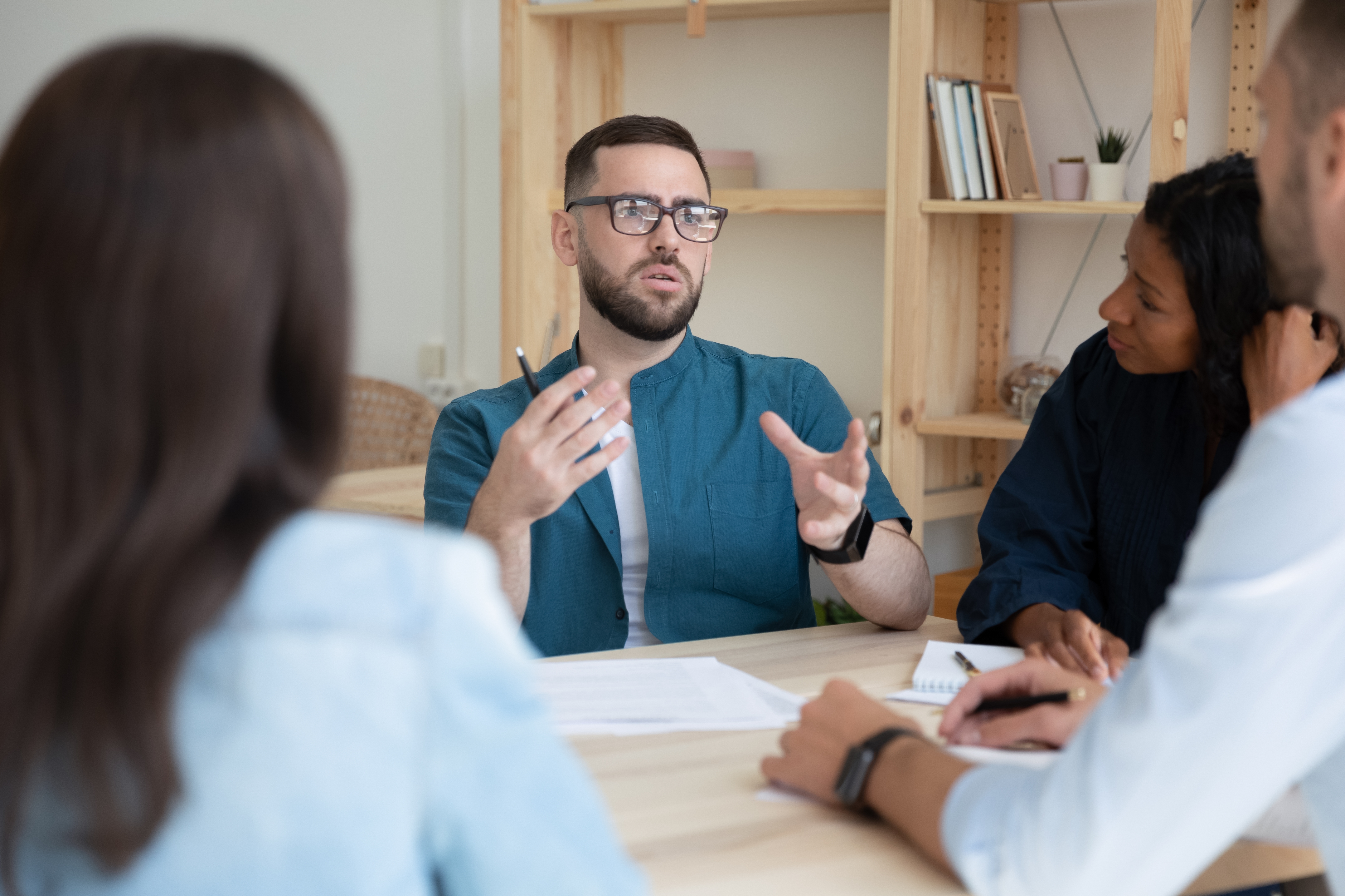 Instructor sitting across a table from his students and talking to them in a foreign language