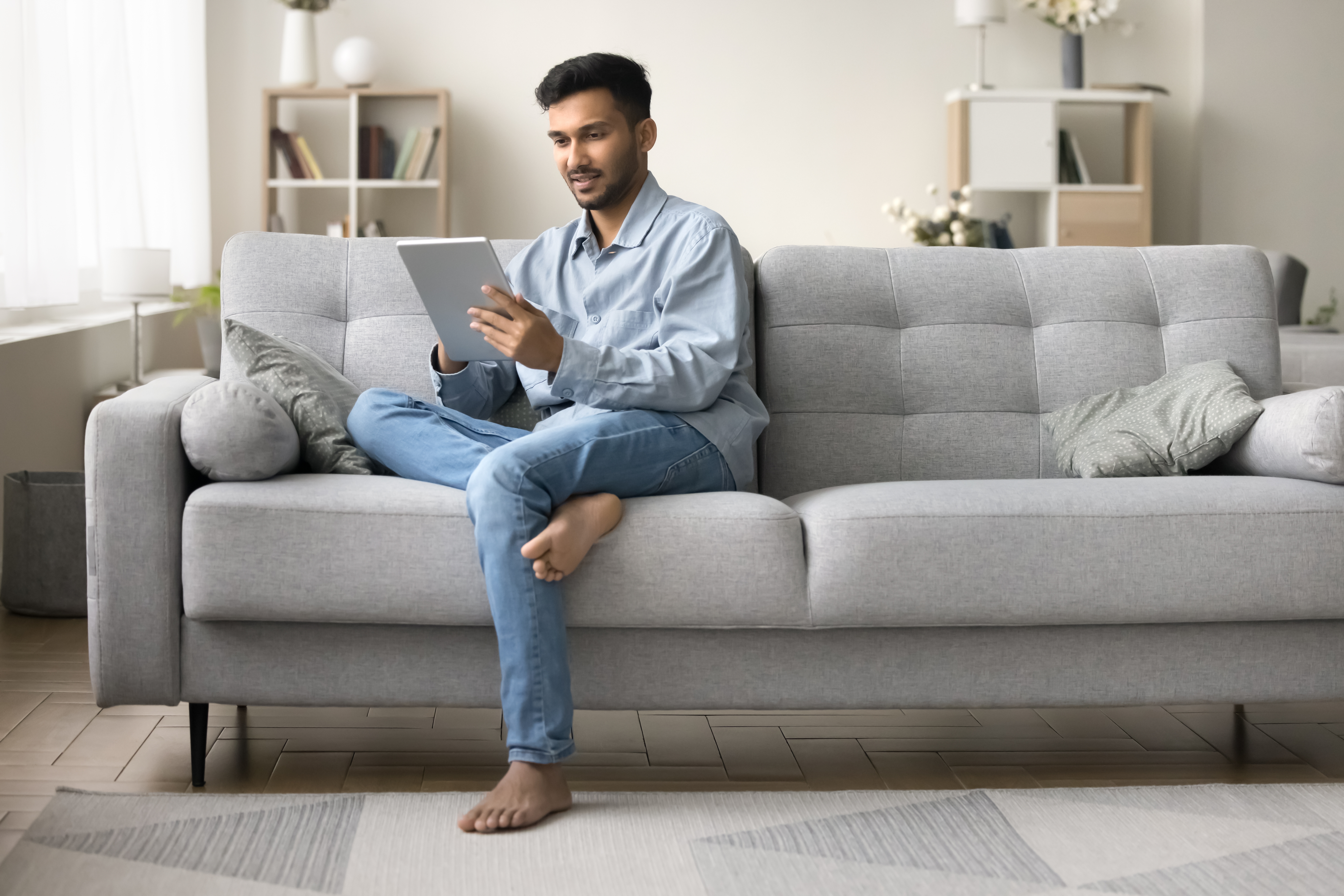 Man sitting on a couch holding a tablet and joining his private online language class with Berlitz