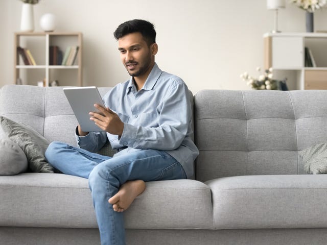 Man sitting on a couch holding a tablet and joining his private online language class with Berlitz