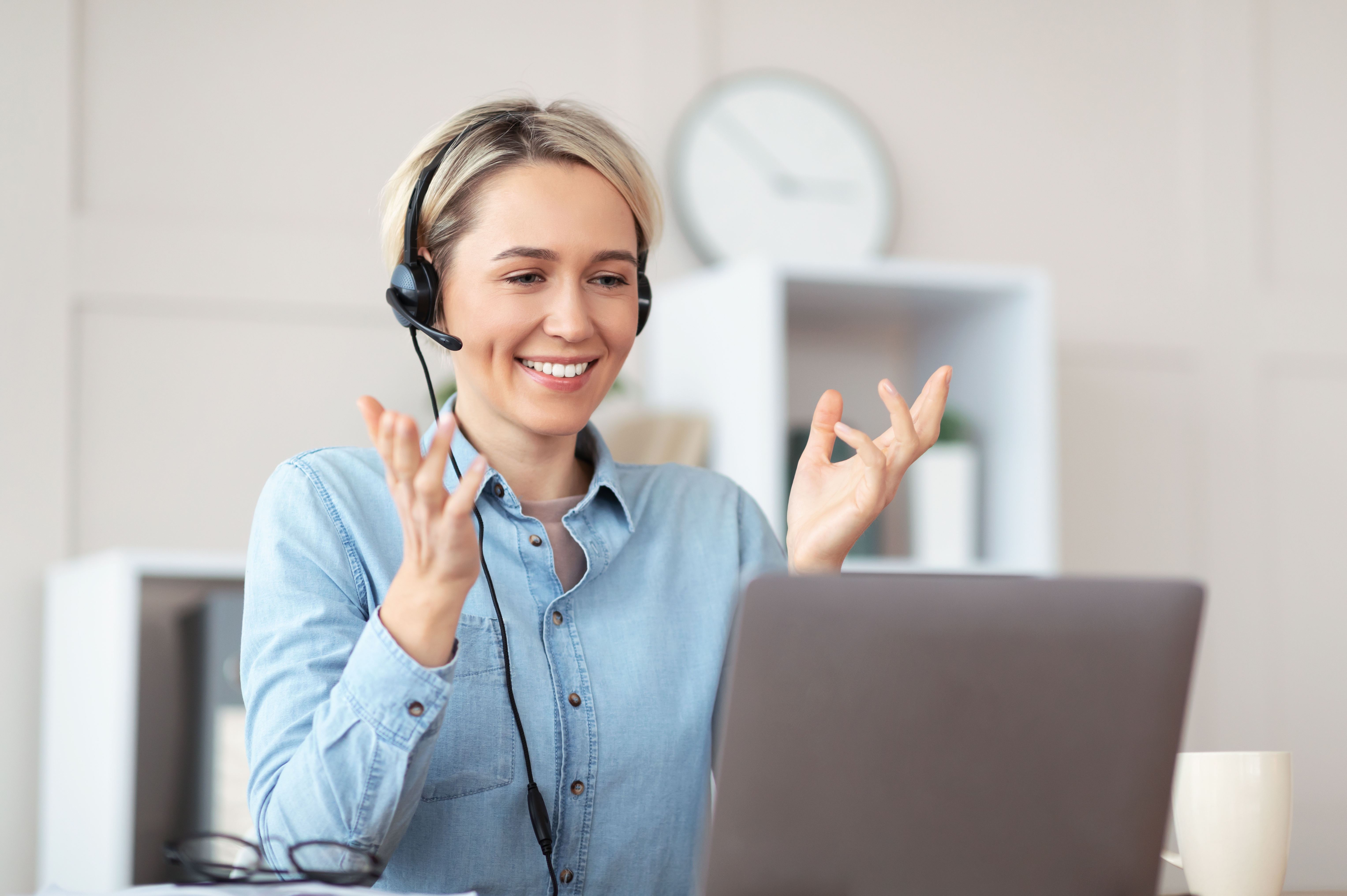 Woman in headphones attending an online private language class from her laptop and talking to her instructor in a foreign language