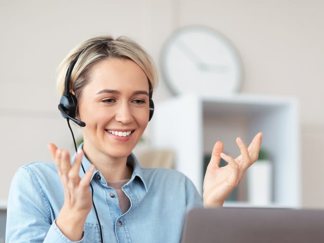 Woman in headphones attending an online private language class from her laptop and talking to her instructor in a foreign language