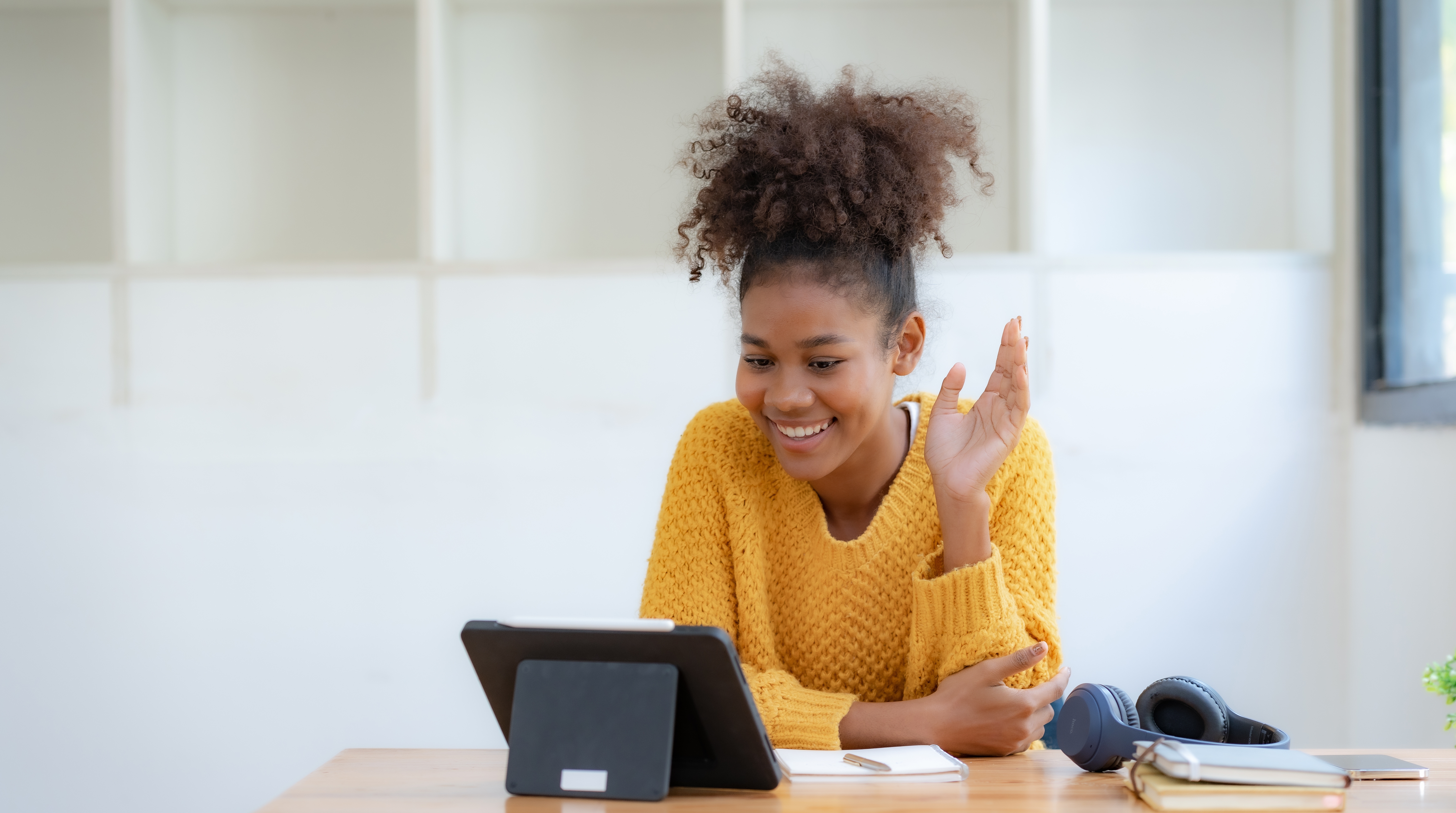 Woman in front of a laptop waving and saying hi to her instructor at the beginning of her online language lesson