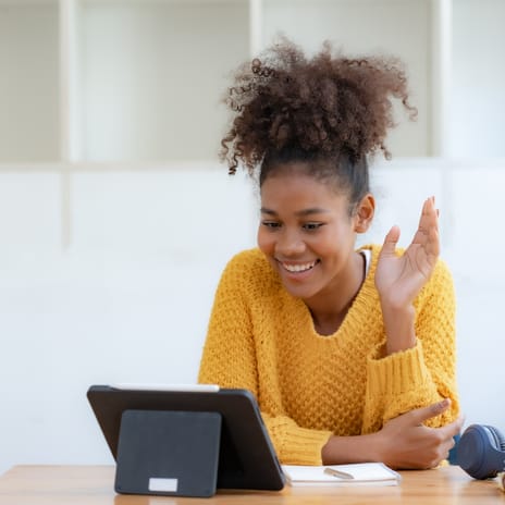 Woman in front of a laptop waving and saying hi to her instructor at the beginning of her online language lesson