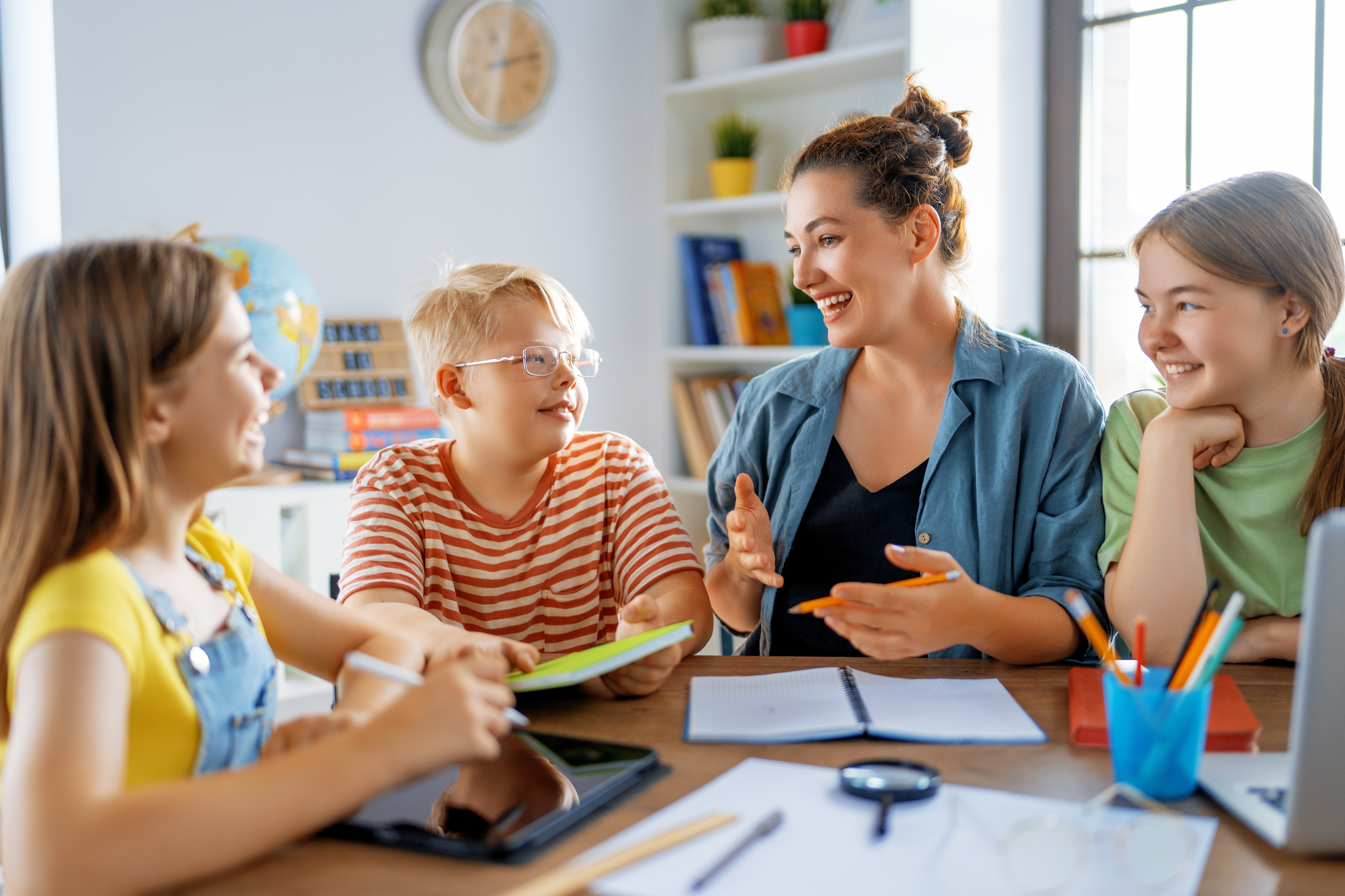 Instructor sitting next to kids at a table and talking to them in Spanish during their Spanish courses for kids and teens