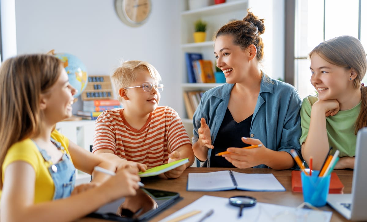 Instructor sitting next to kids at a table and talking to them in Spanish during their Spanish courses for kids and teens