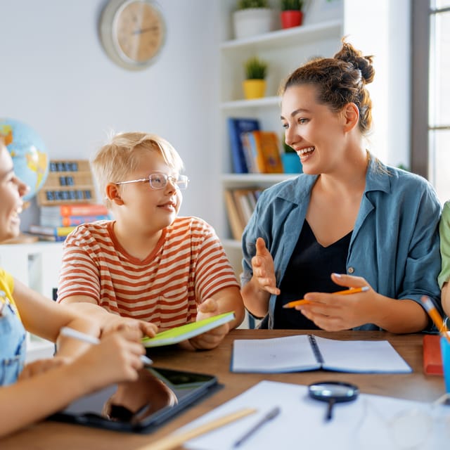 Instructor sitting next to kids at a table and talking to them in Spanish during their Spanish courses for kids and teens