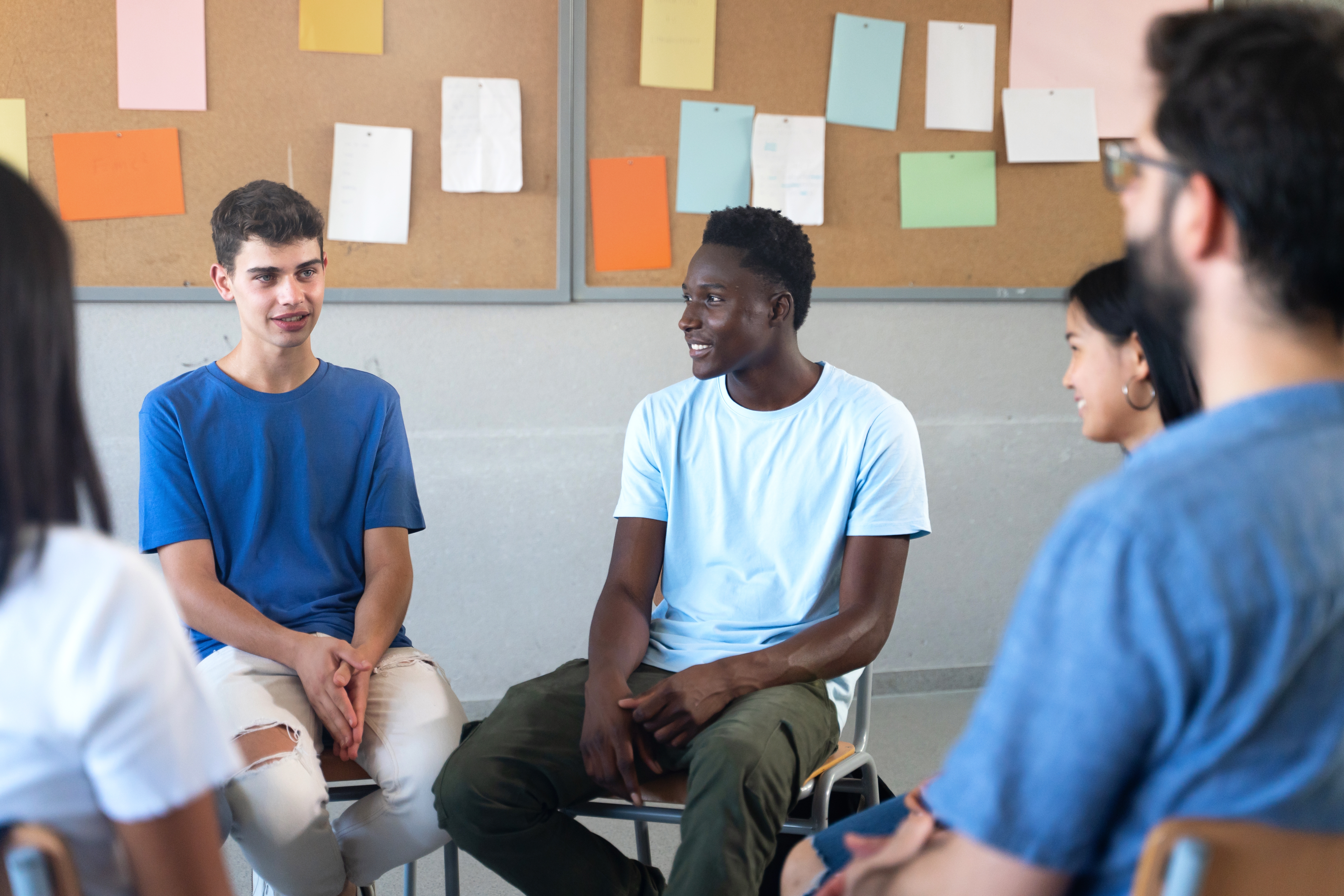 Teenagers sitting in a circle in front of a note board and talking to each other and their instructor during a lesson with Berlitz where they learn Spanish for kids and teens