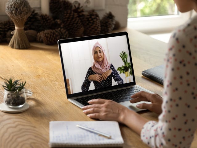 Woman with headphones attending an online private language course from her laptop and making notes
