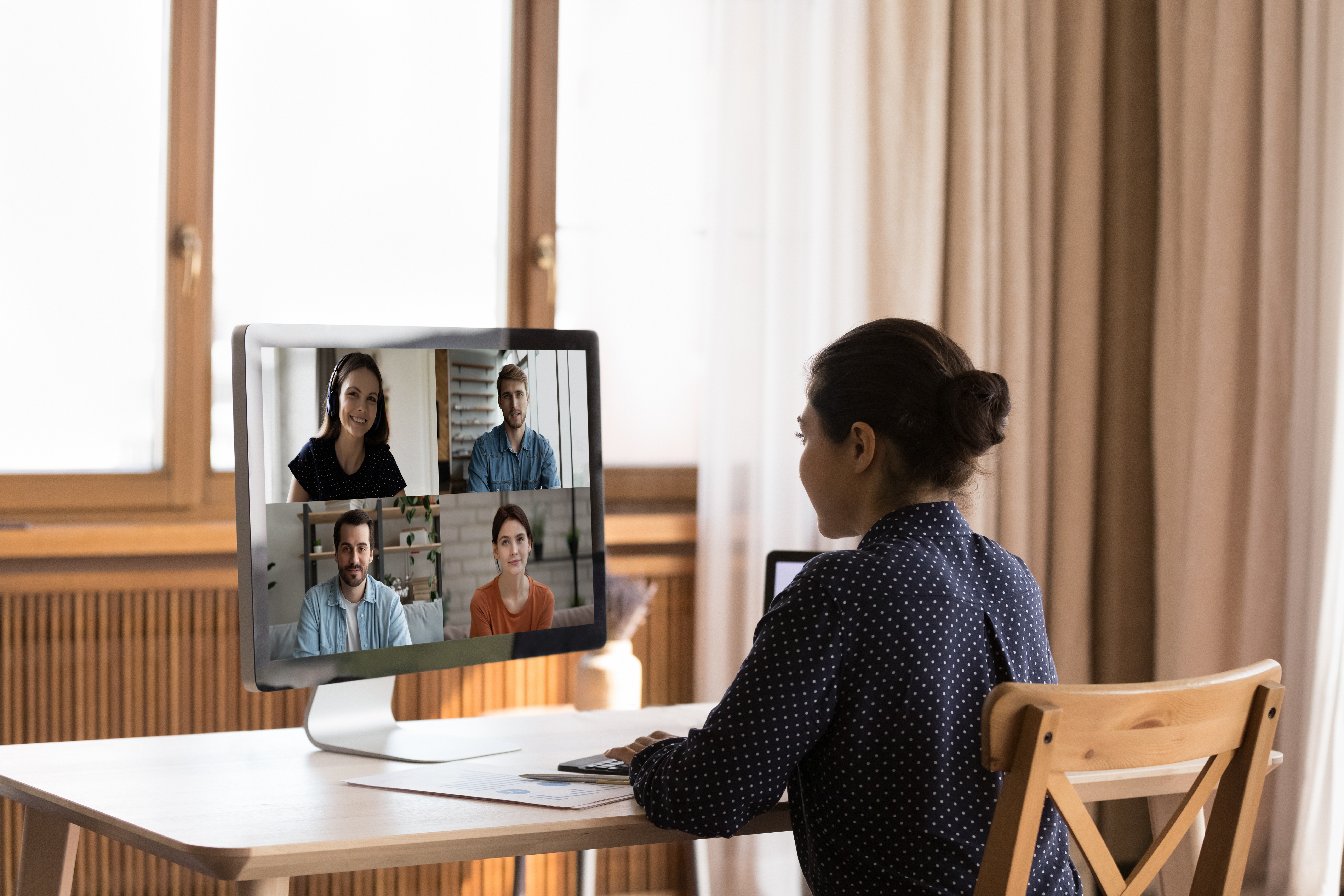 Woman sitting at a table in front of a computer and attending an online group language lesson