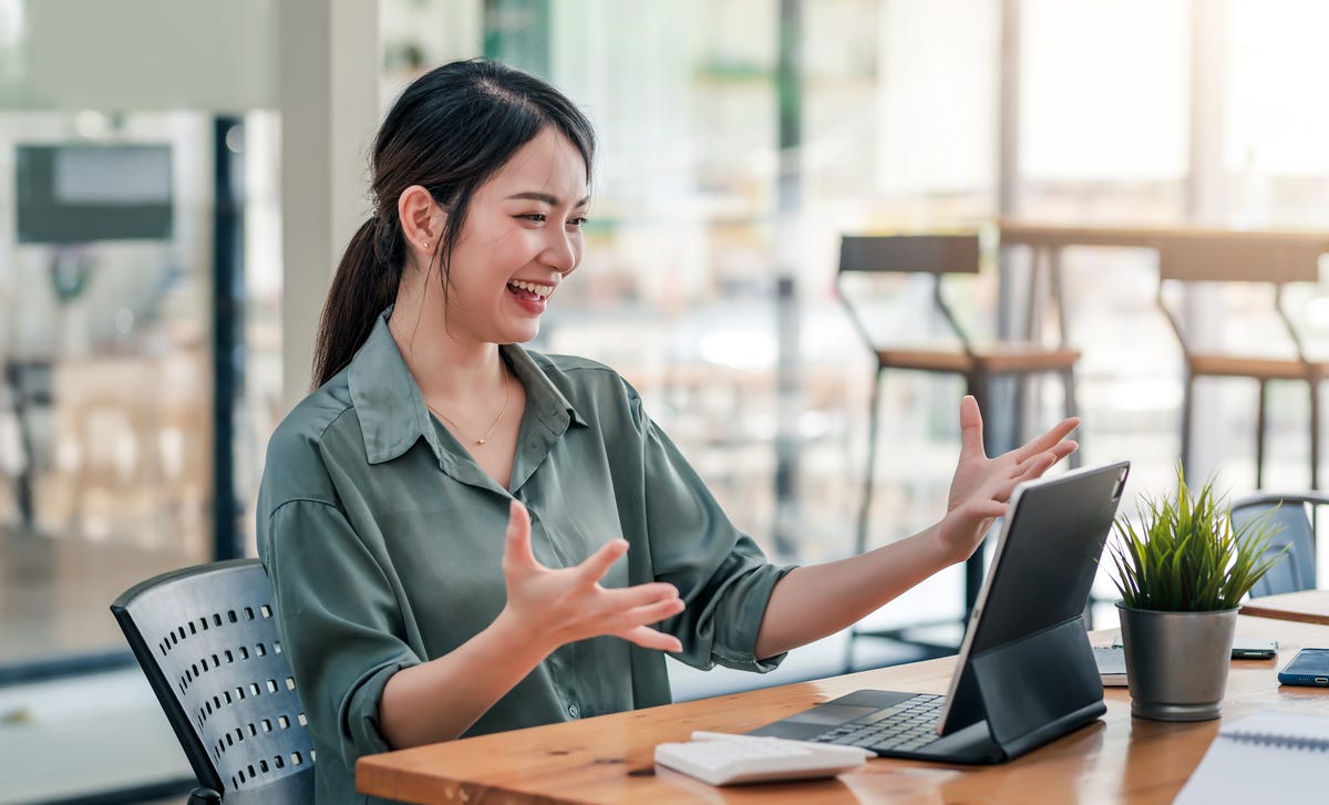 Woman sitting in front of a laptop and happily greeting her instructor before she starts to learn English online
