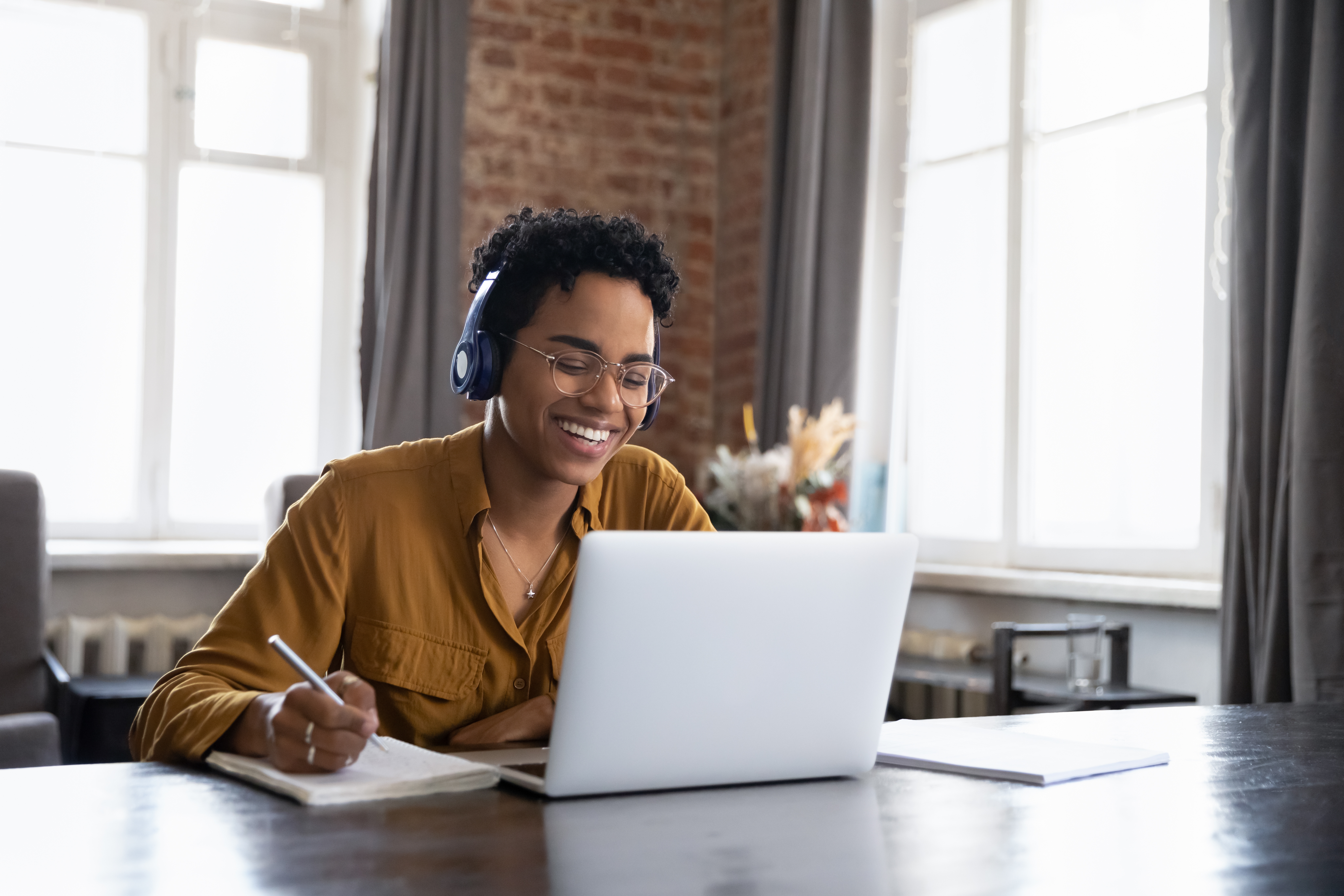 Woman with headphones holding a pen and making a notes during online language learning