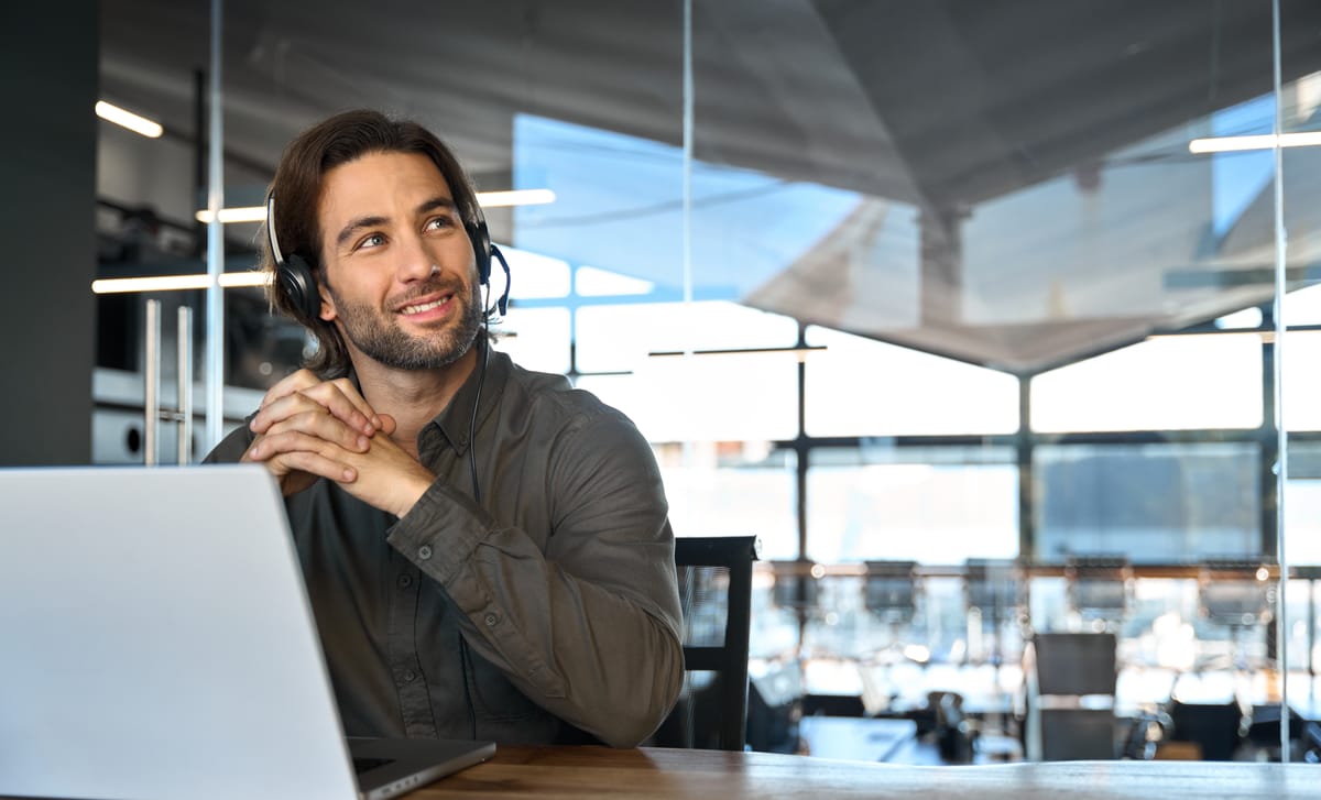 Man with headphones sitting in front of a computer and thinking about his answers to the online placement test