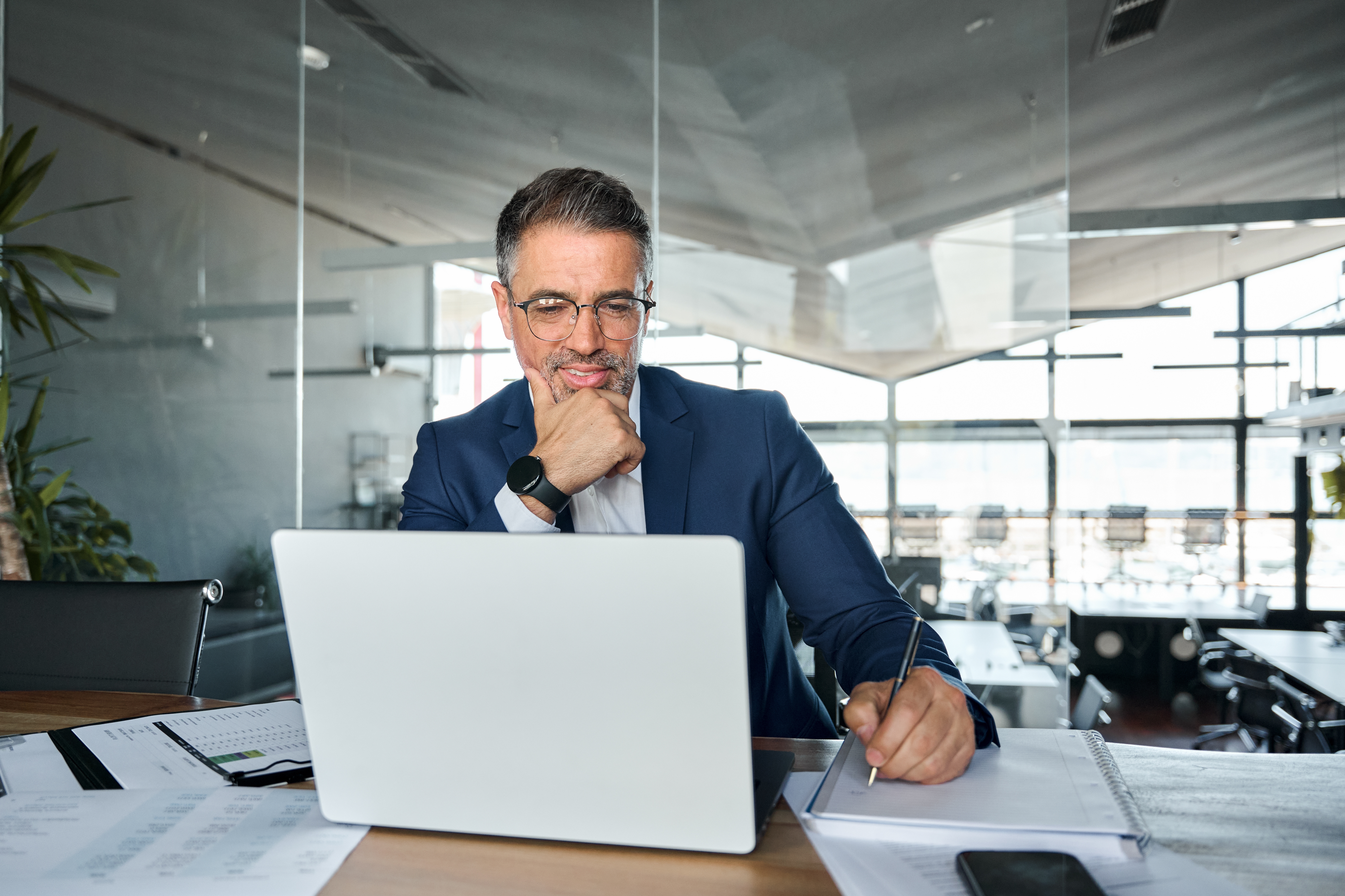 Businessman in front of a laptop holding a pen and making notes during his self-paced language course