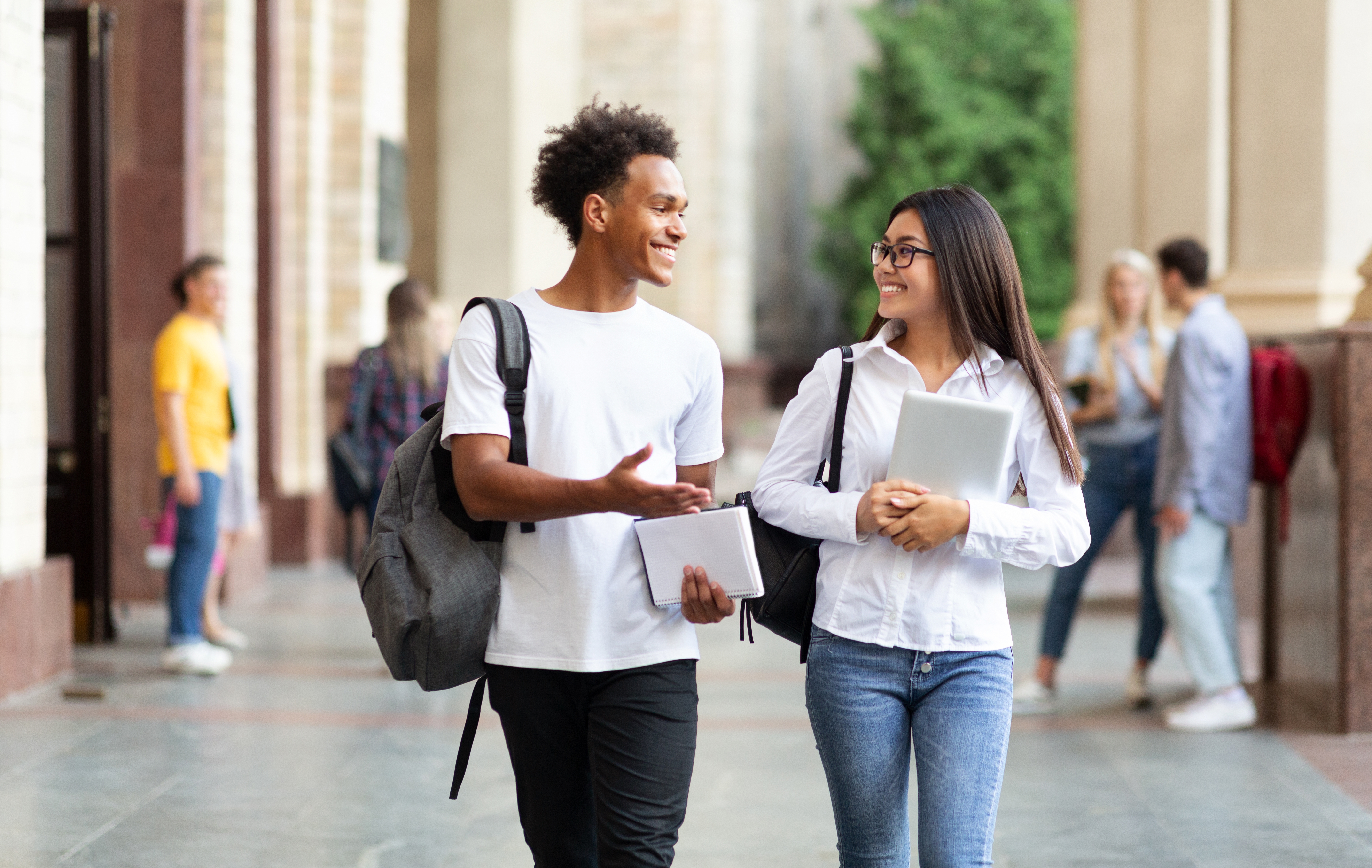 Twi teenagers holding notes and talking to each other while smiling after their French courses for kids and teens