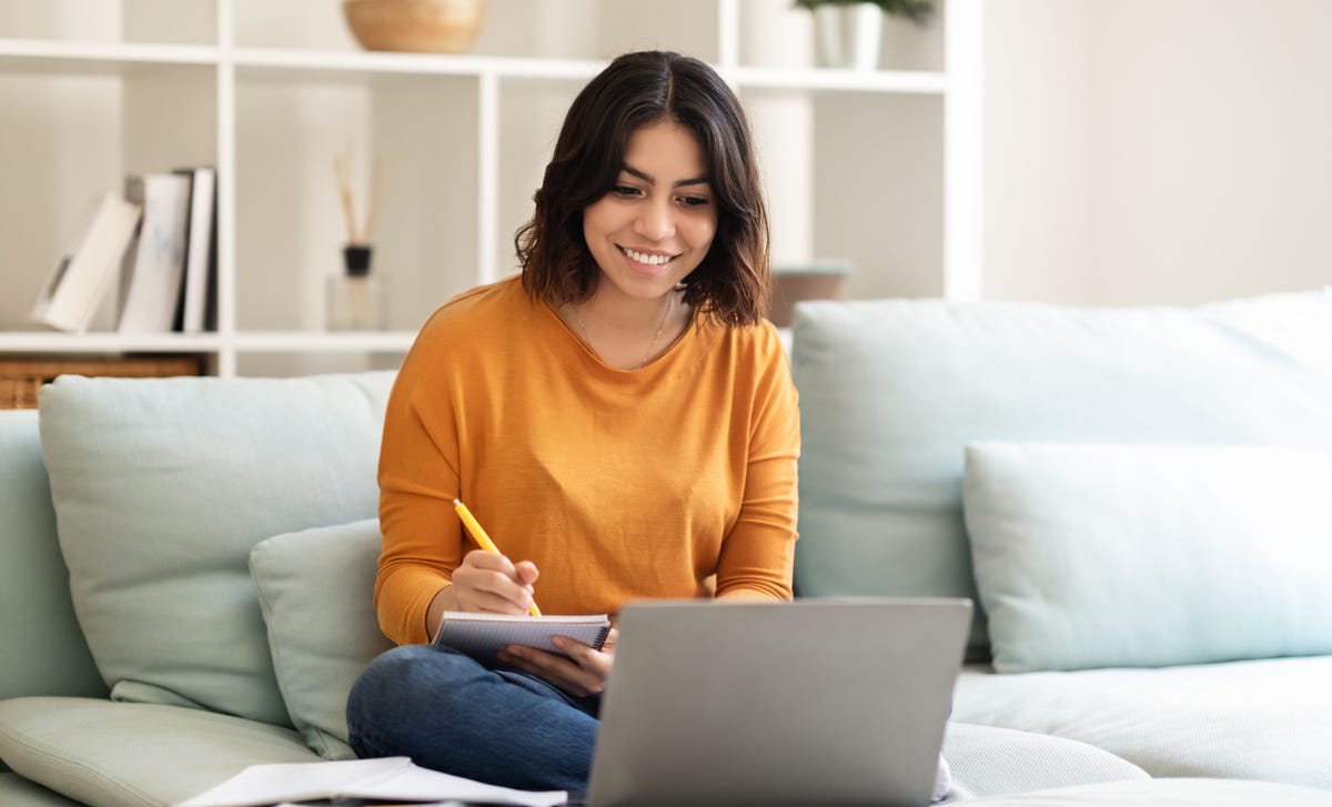 Woman with a notepad sitting in front of a computer and reading about why it's beneficial for her to learn a language with Berlitz