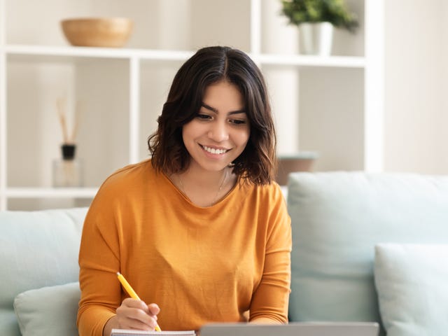 Woman with a notepad sitting in front of a computer and reading about why it's beneficial for her to learn a language with Berlitz