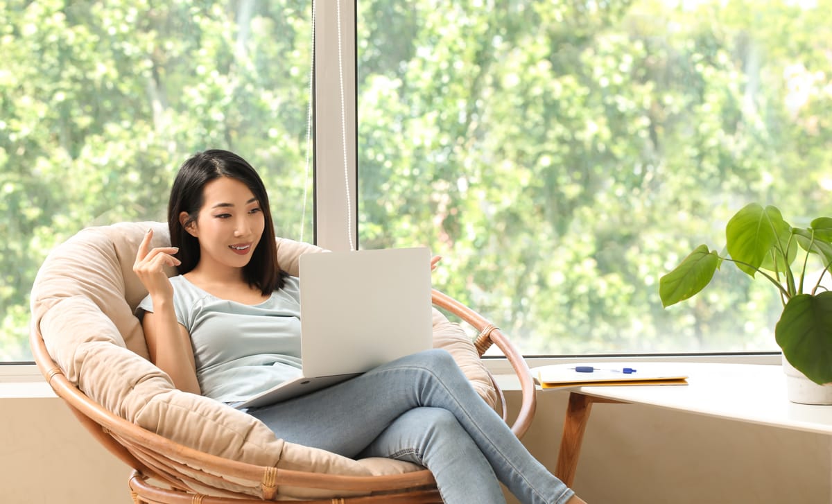 Woman sitting in an armchair and reading about the history of Berlitz on her laptop