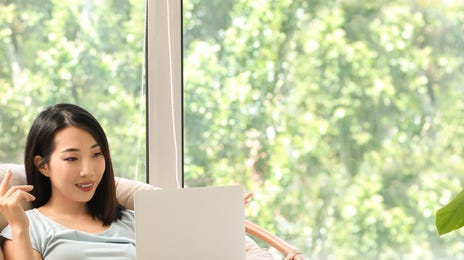 Woman sitting in an armchair and reading about the history of Berlitz on her laptop