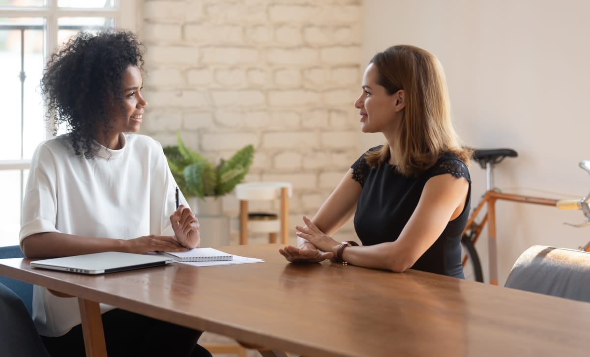 Two women sitting at a table and talking to each other happily in a foreign language during an intensive language class with Berlitz