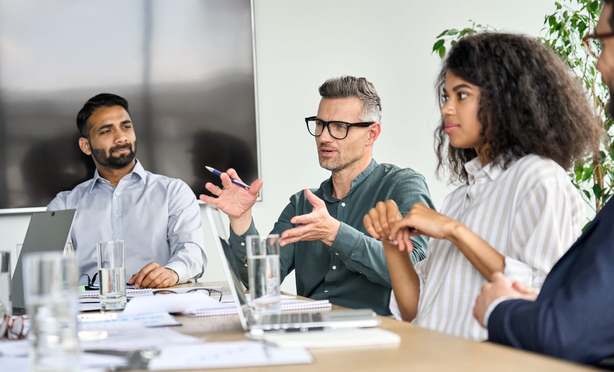 A team leader talking to his team members sitting around a table after he learned about business communication for professionals with Berlitz
