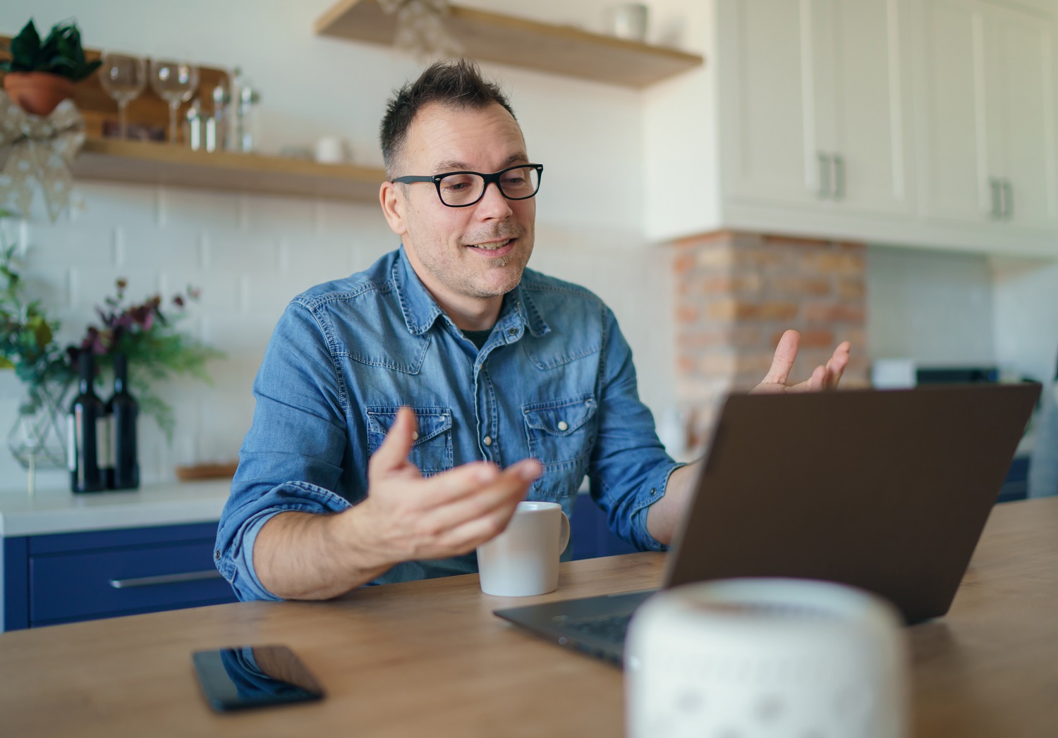 Man sitting at the counter in his kitchen with a cup of tea and talking to his instructor during an online English lesson with Berlitz Czechia