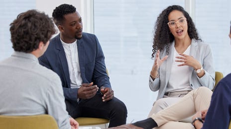 Group os students sitting on chairs in a circle and talking to their instructor