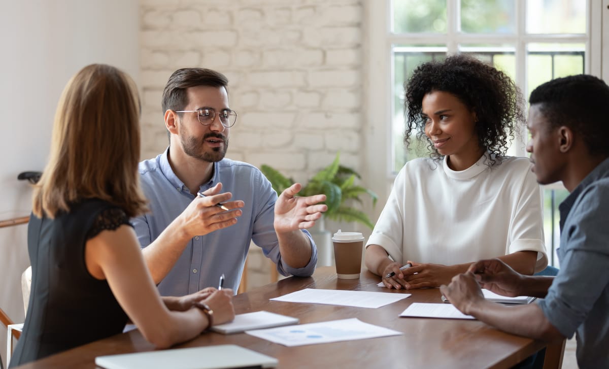 Students sitting around a table and talking to each other and their instructor to learn Italian