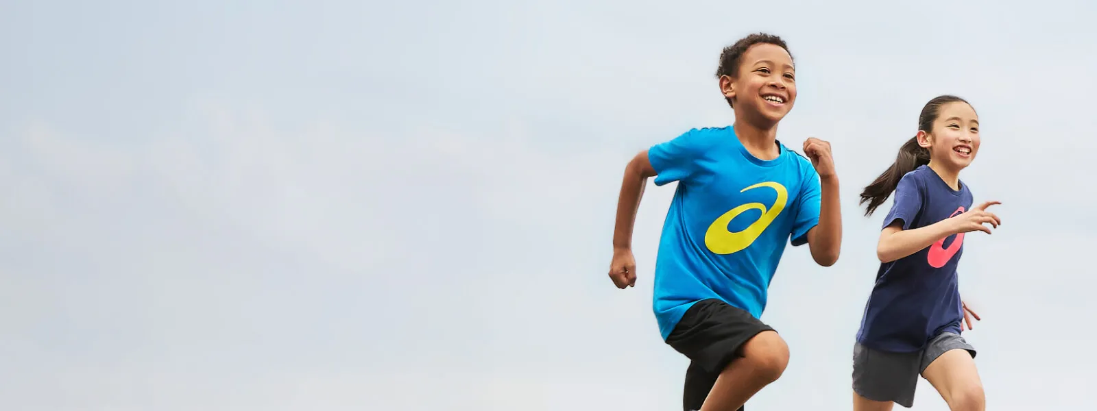 Two kids running in ASICS gear outside with a blue background.