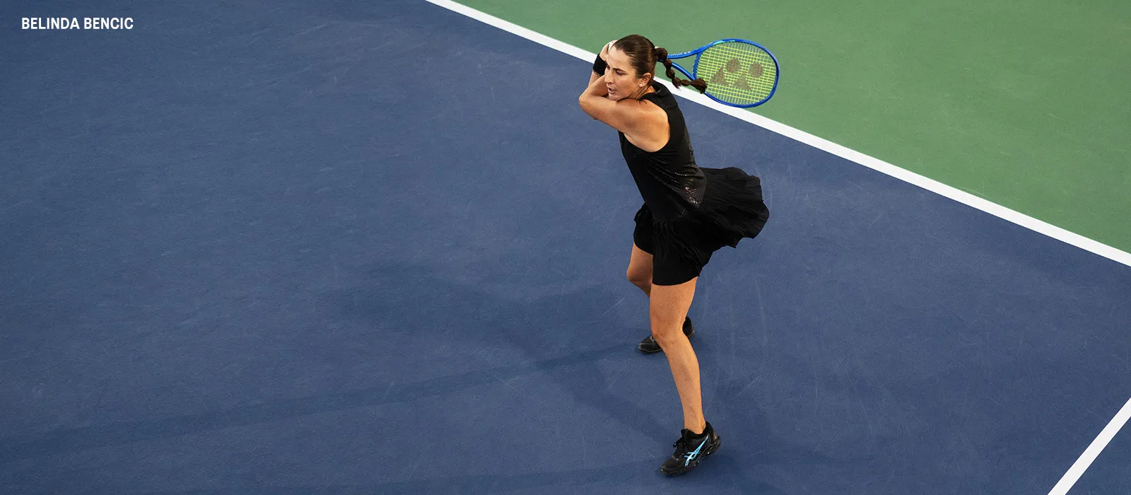 Athlete belinda bencic playing tennis wearing a black dress and black tennis shoes.