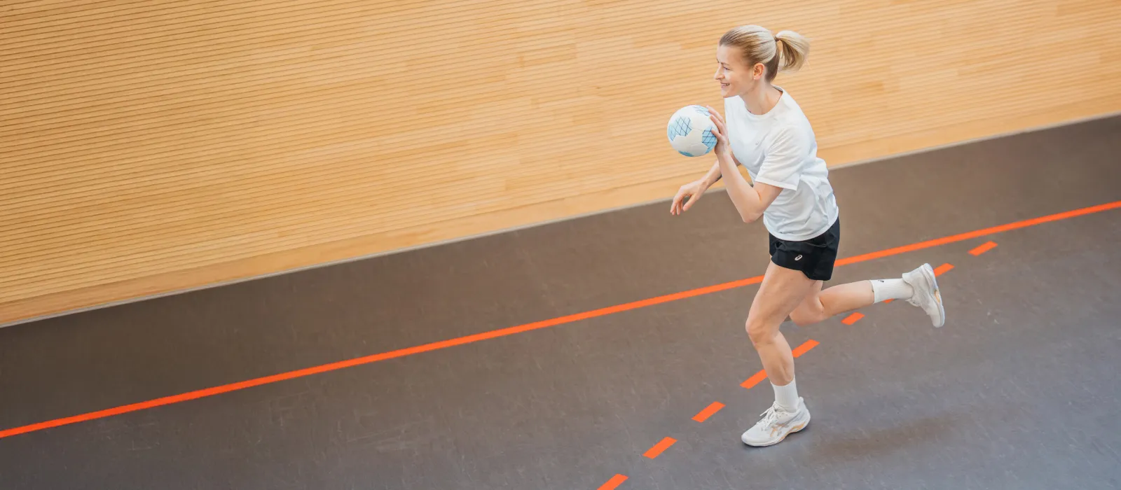 Woman running with a handball while wearing ASICS handball shoes and clothing.