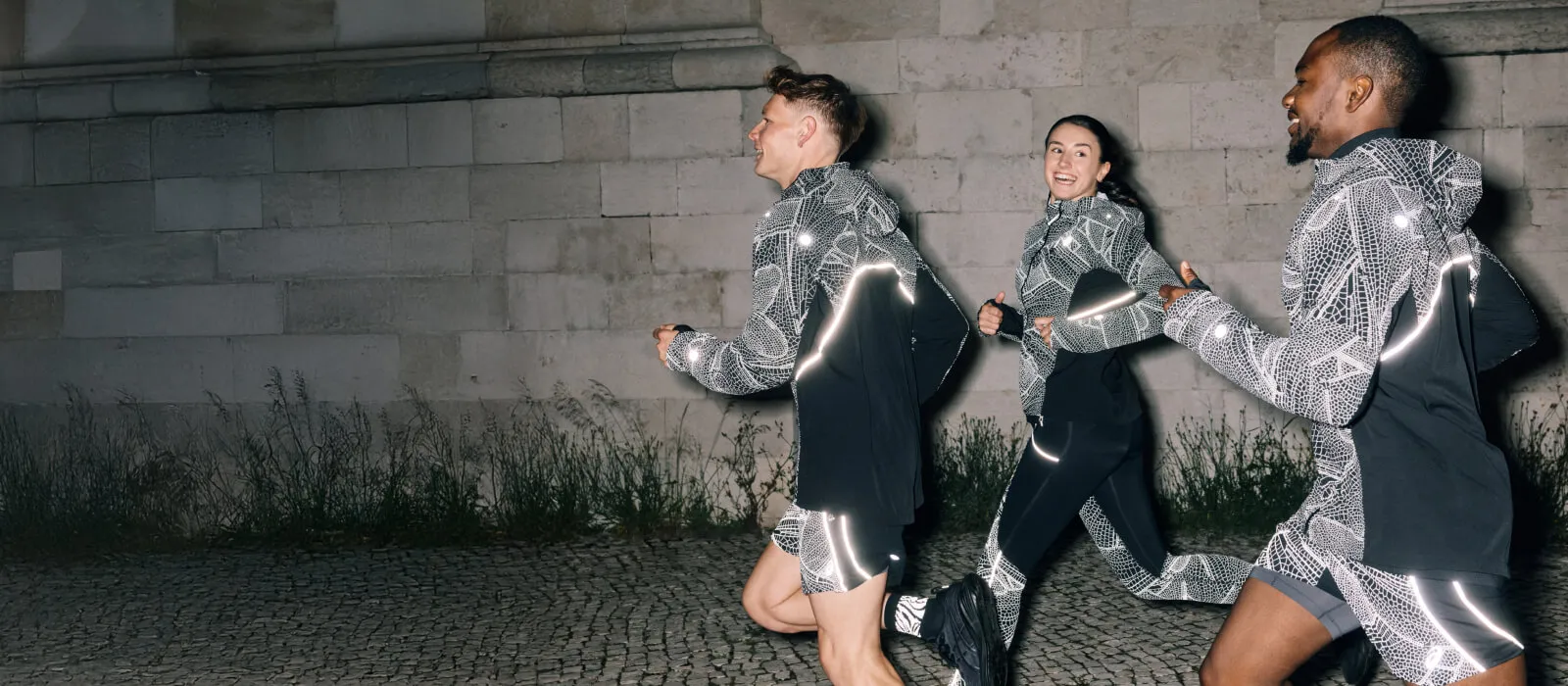 Three runners, two men and one woman running at night in the city wearing limited series reflective running apparel for visibility.