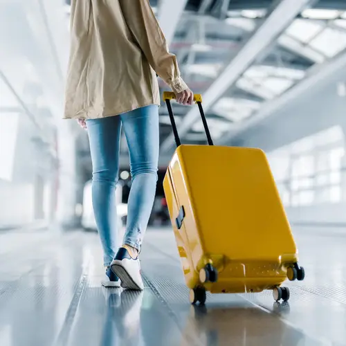 Woman traveling down airport with a yellow suitcase