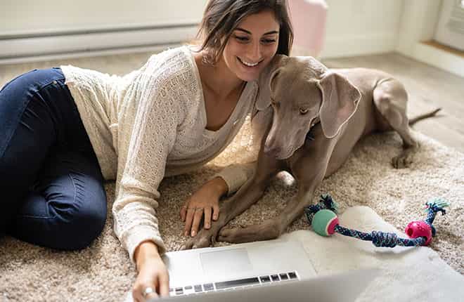 A woman laying on the floor with a dog and a laptop.