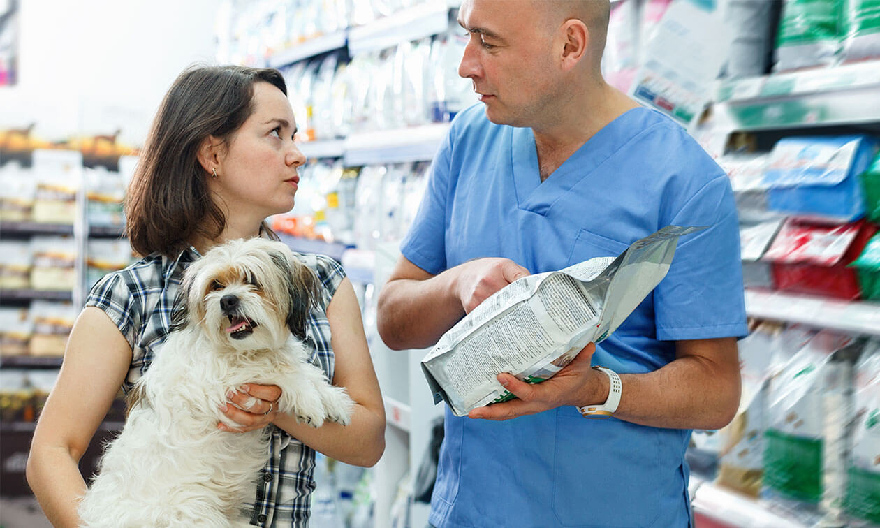 A woman holding a dog discusses dog food with a veterinarian.
