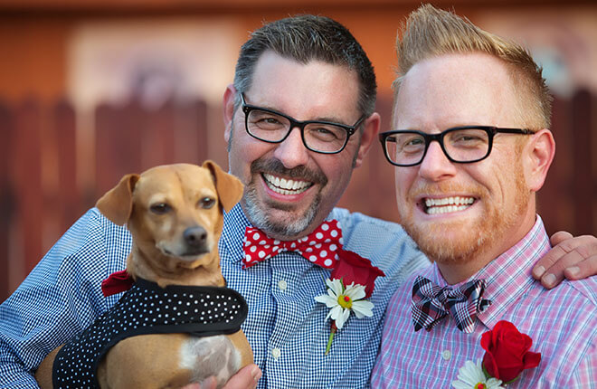 A couple of men standing next to each other holding a dog.