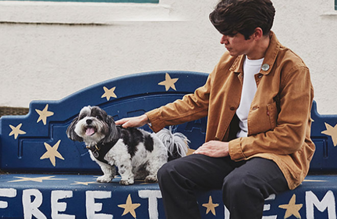 A man sitting on a bench petting a dog.