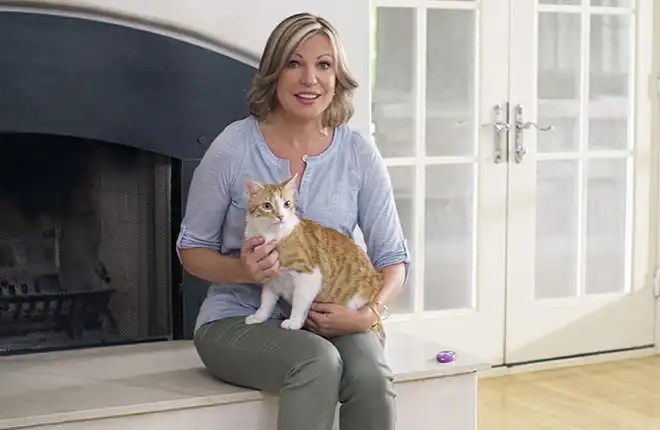 A woman sitting on a fireplace holding a cat.