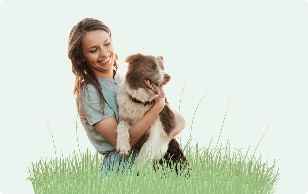 A woman holding a dog in a grassy field.