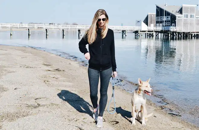 A woman walking a dog on a leash on the beach.