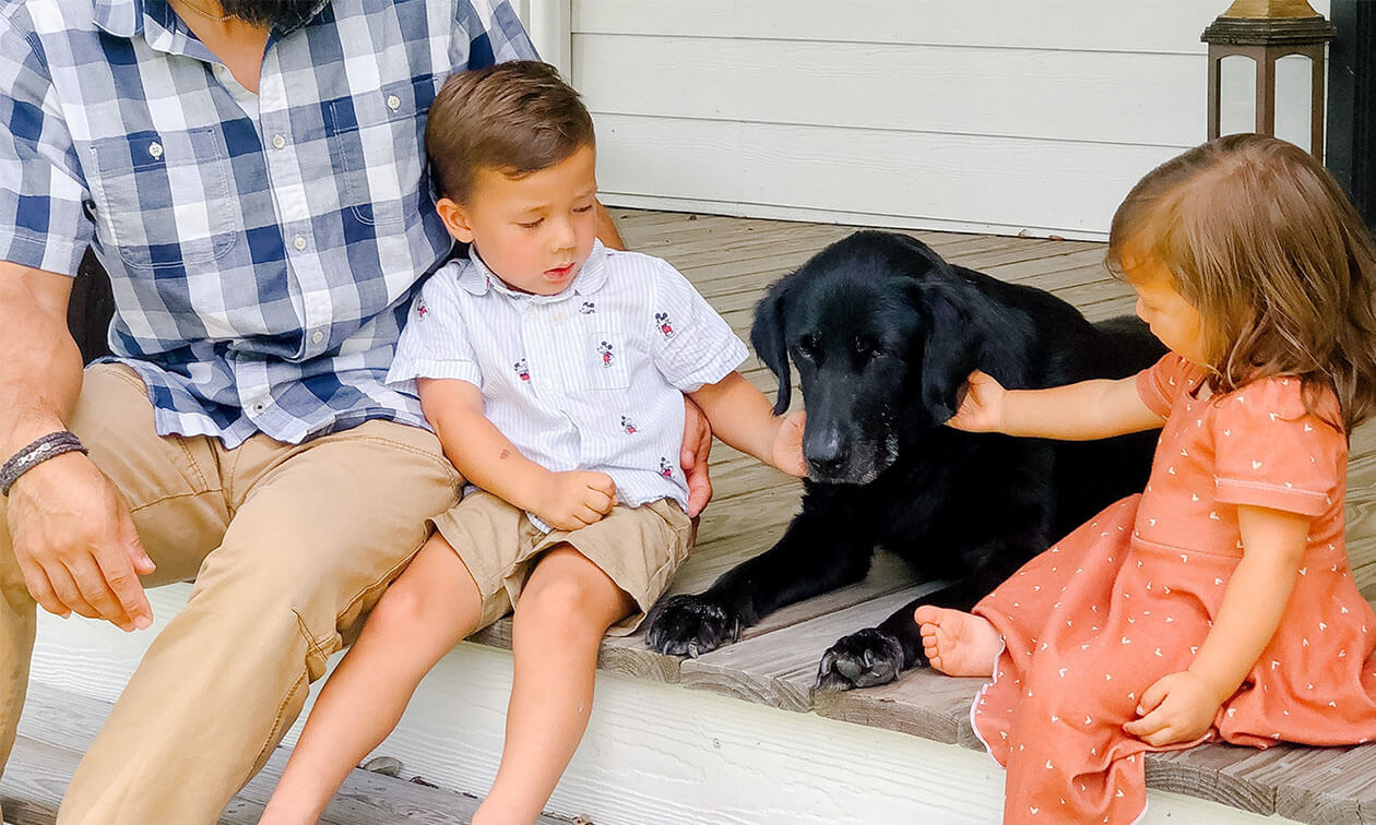 A man sitting on a porch with two children and a dog.