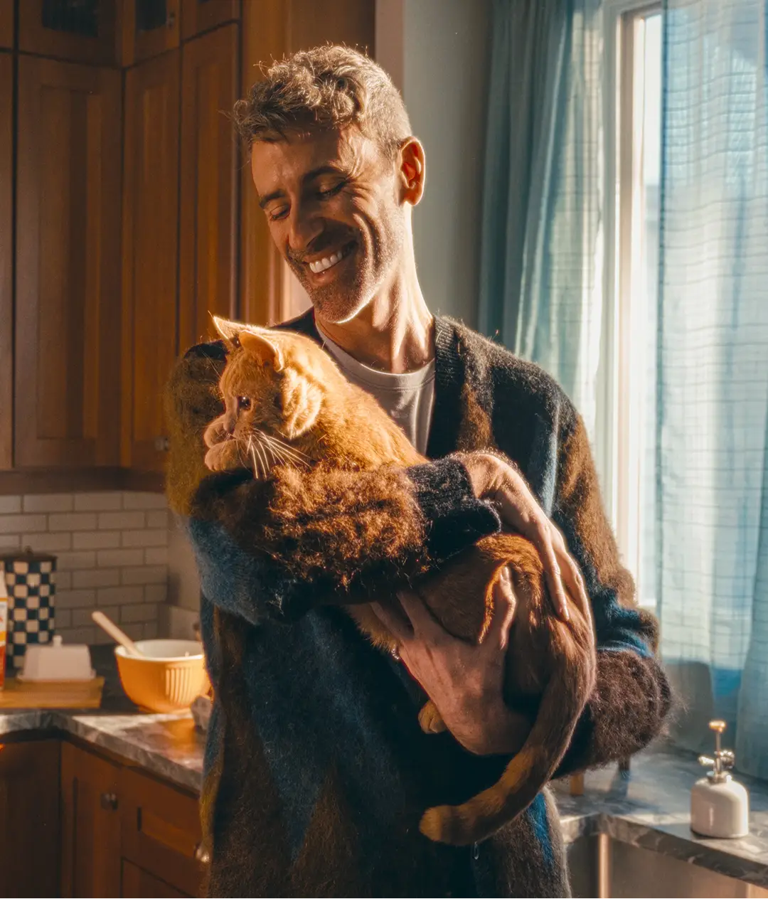 Man standing in kitchen holding is cat and smiling