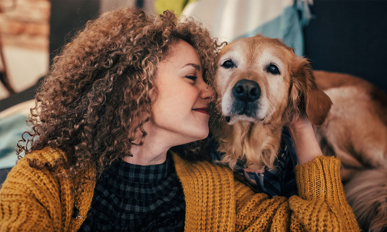 A woman with curly hair is hugging a dog.