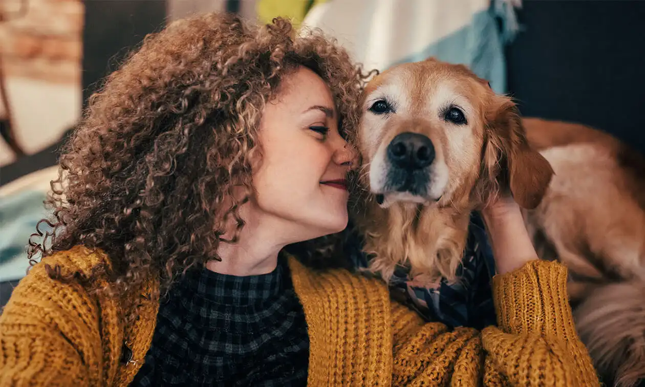 A woman with curly hair is hugging a dog.