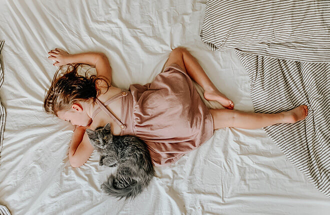 A little girl laying on a bed with a cat.