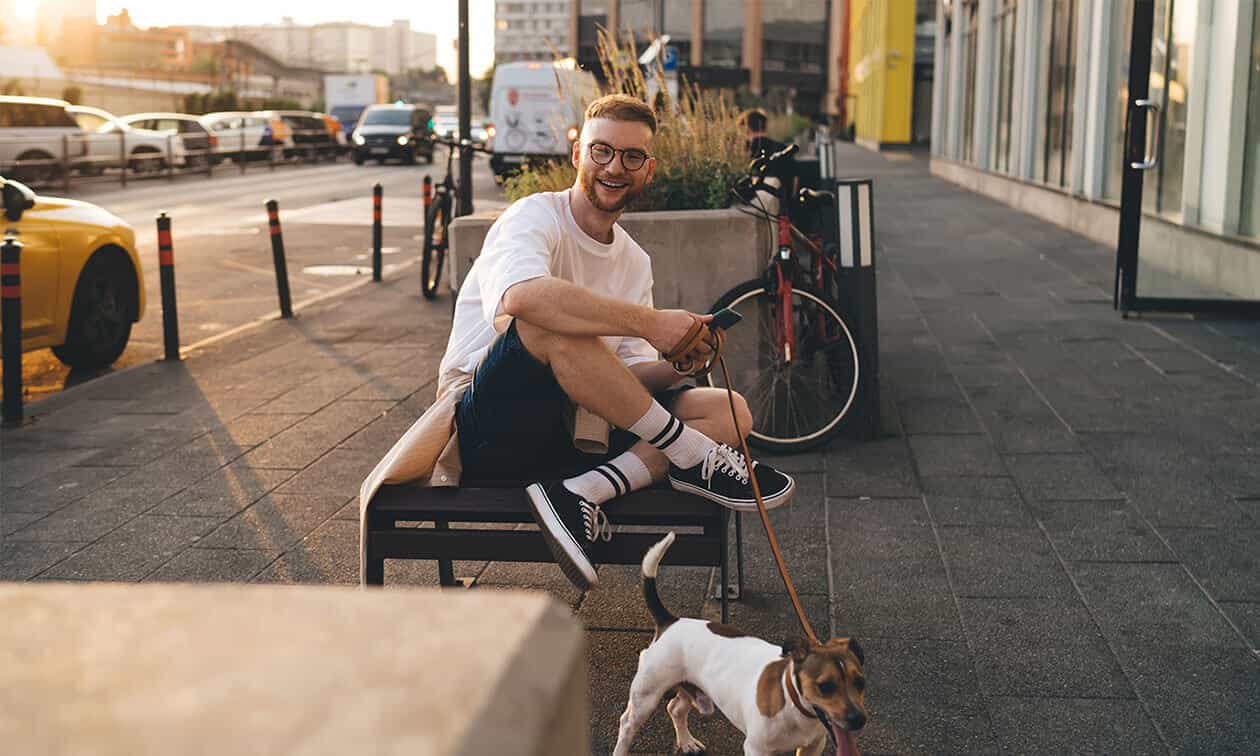 A man sitting on a bench with a dog on a leash.