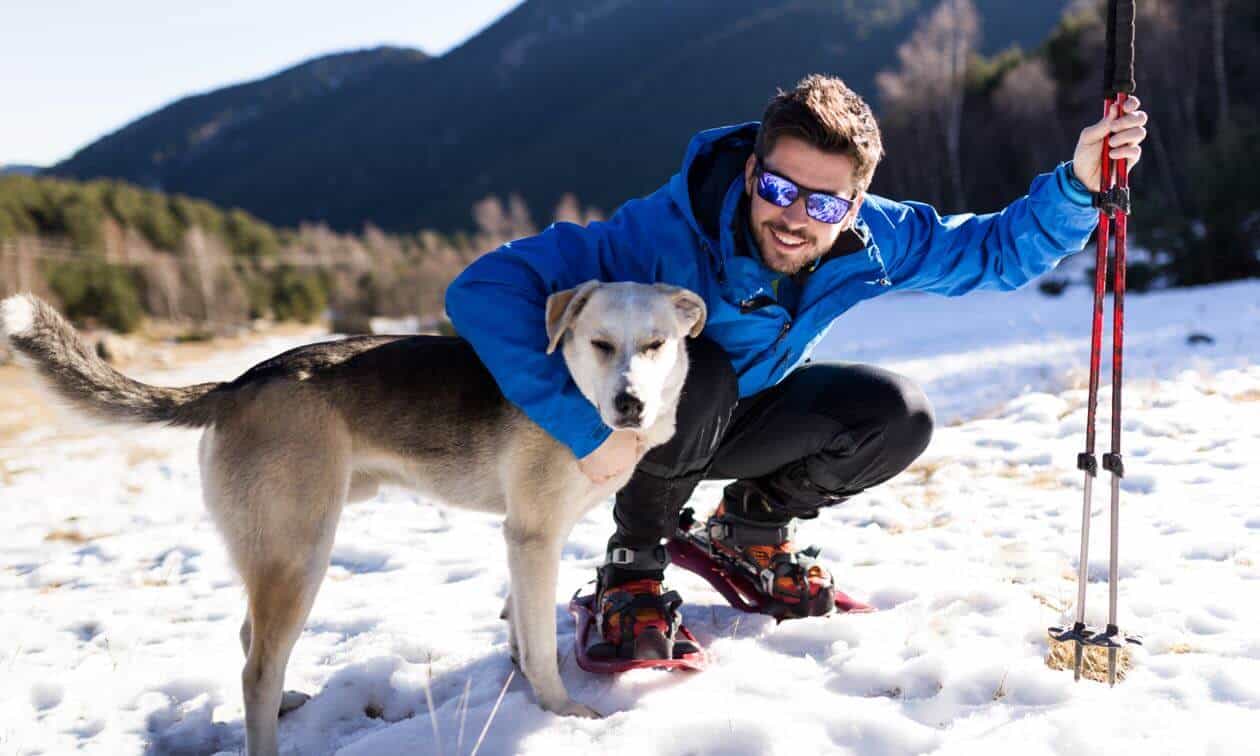 A man kneeling down next to a dog in the snow.