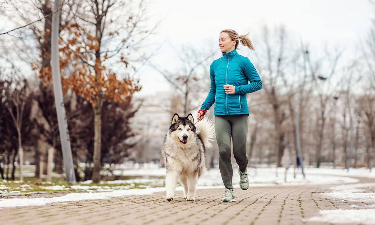 A woman jogging with her dog in the snow.