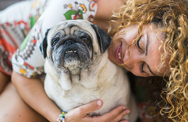 A woman is hugging a pug dog.
