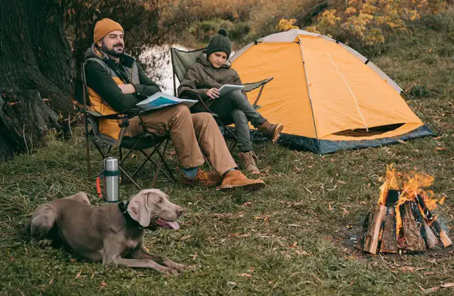 A couple of people sitting in chairs next to a fire.